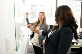 2 Smiling Women Writing on a Large White Board