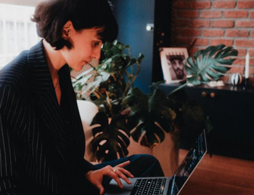 Woman Wearing a Black Blazer and Typing on a Silver Laptop