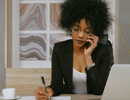 African American Woman with Short Hair and Glasses Talking on a Smartphone and Sitting at a Desk