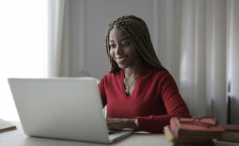 Smiling African American Woman with Long Hair Smiling at a Laptop Screen