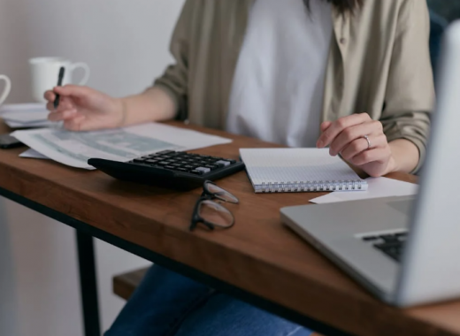 Woman Sitting at a Desk with a Laptop, Writing Tablet, and Calculator