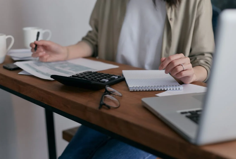 Woman Sitting at a Desk with a Laptop, Writing Tablet, and Calculator