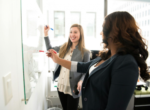2 Smiling Women Writing on a Whiteboard