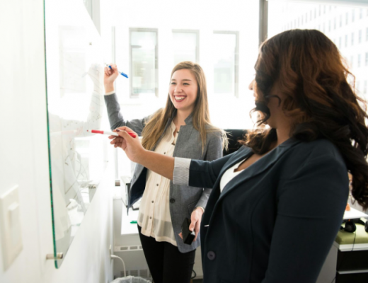2 Smiling Women Writing on a Whiteboard