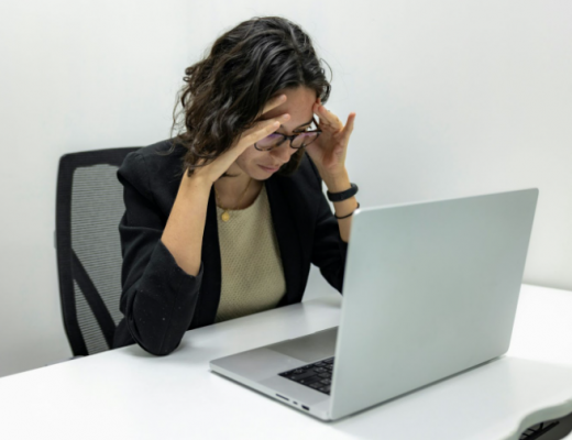 Woman Holding Her Head in Her Hands While Sitting at Her Desk