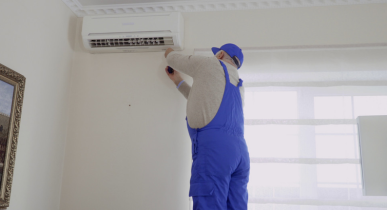 Man Wearing Blue Overalls Working on a Wall HVAC Unit