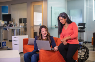2 Smiling Women Sitting at a Couch and Smiling at a Laptop