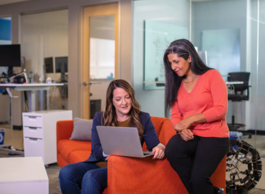 2 Smiling Women Sitting at a Couch and Smiling at a Laptop