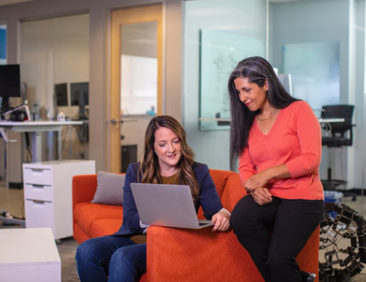 2 Smiling Women Sitting at a Couch and Smiling at a Laptop