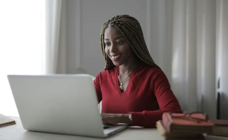 Smiling African American Woman with Long Hair Smiling at a Laptop Screen