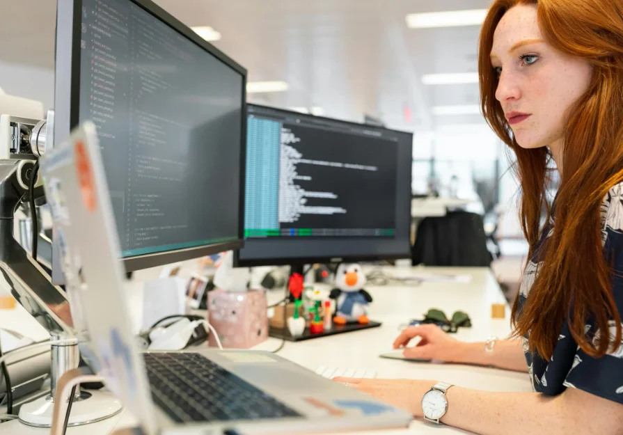 Woman with Long Red Hair Sitting in Front of Computer Monitors