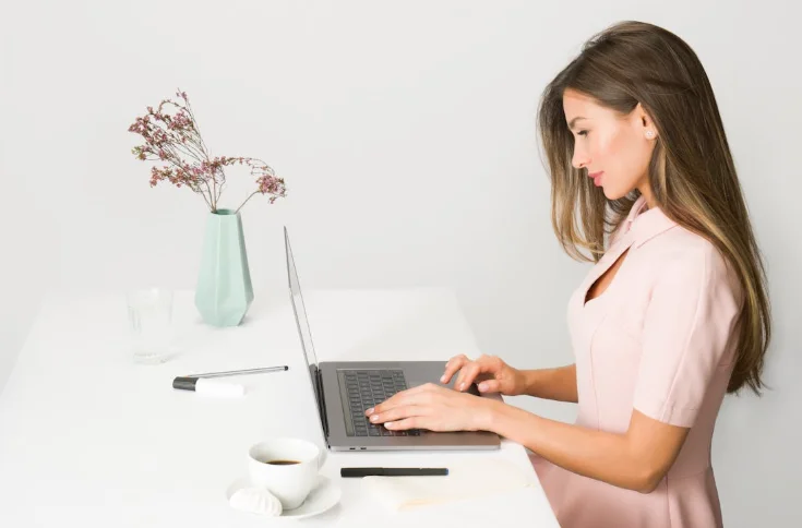 Side Profile of a Woman Wearing a Pink Dress and Typing on a Laptop