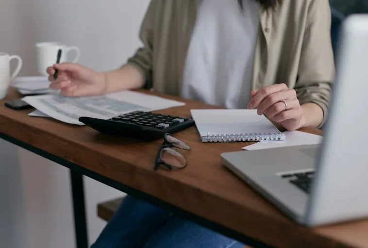 Woman Sitting at a Desk with a Laptop, Writing Tablet, and Calculator