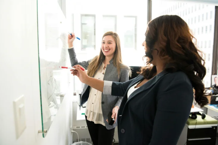 2 Smiling Women Writing on a Whiteboard