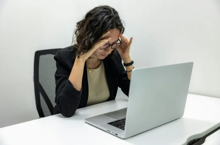 Woman Holding Her Head in Her Hands While Sitting at Her Desk