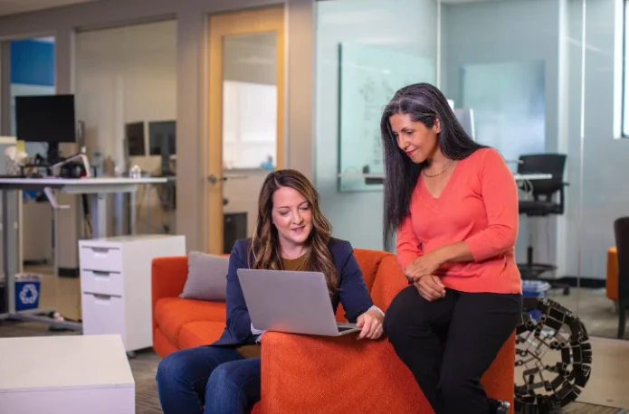 2 Smiling Women Sitting at a Couch and Smiling at a Laptop